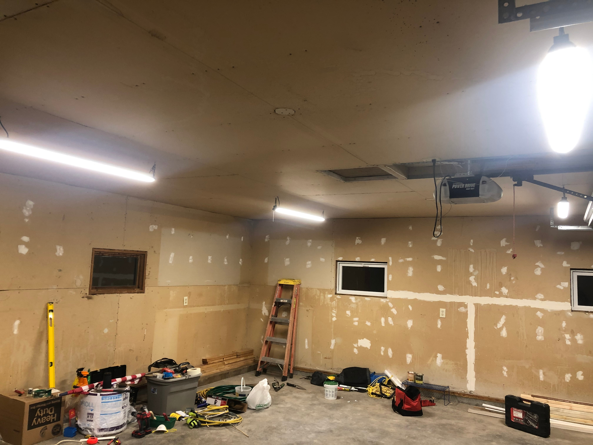 Garage interior mid-repair with patched drywall walls, a repaired ceiling section, and tools staged on the floor