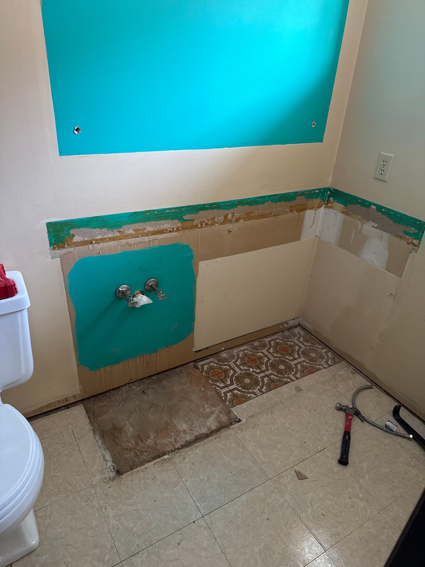 Bathroom mid-demo with vanity removed, exposed drywall patches, teal paint patches, and original tile flooring