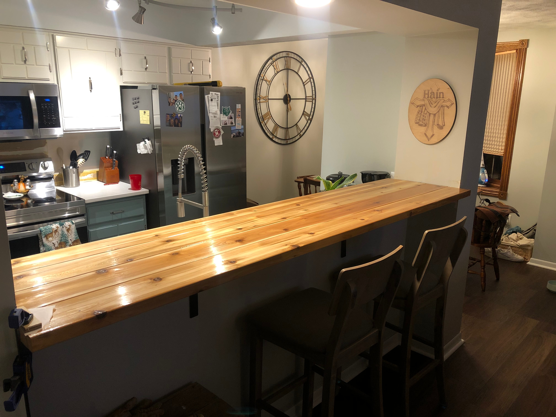 Long cedar plank bar top with a high-gloss clear finish overlooking a kitchen with white cabinets and stainless appliances