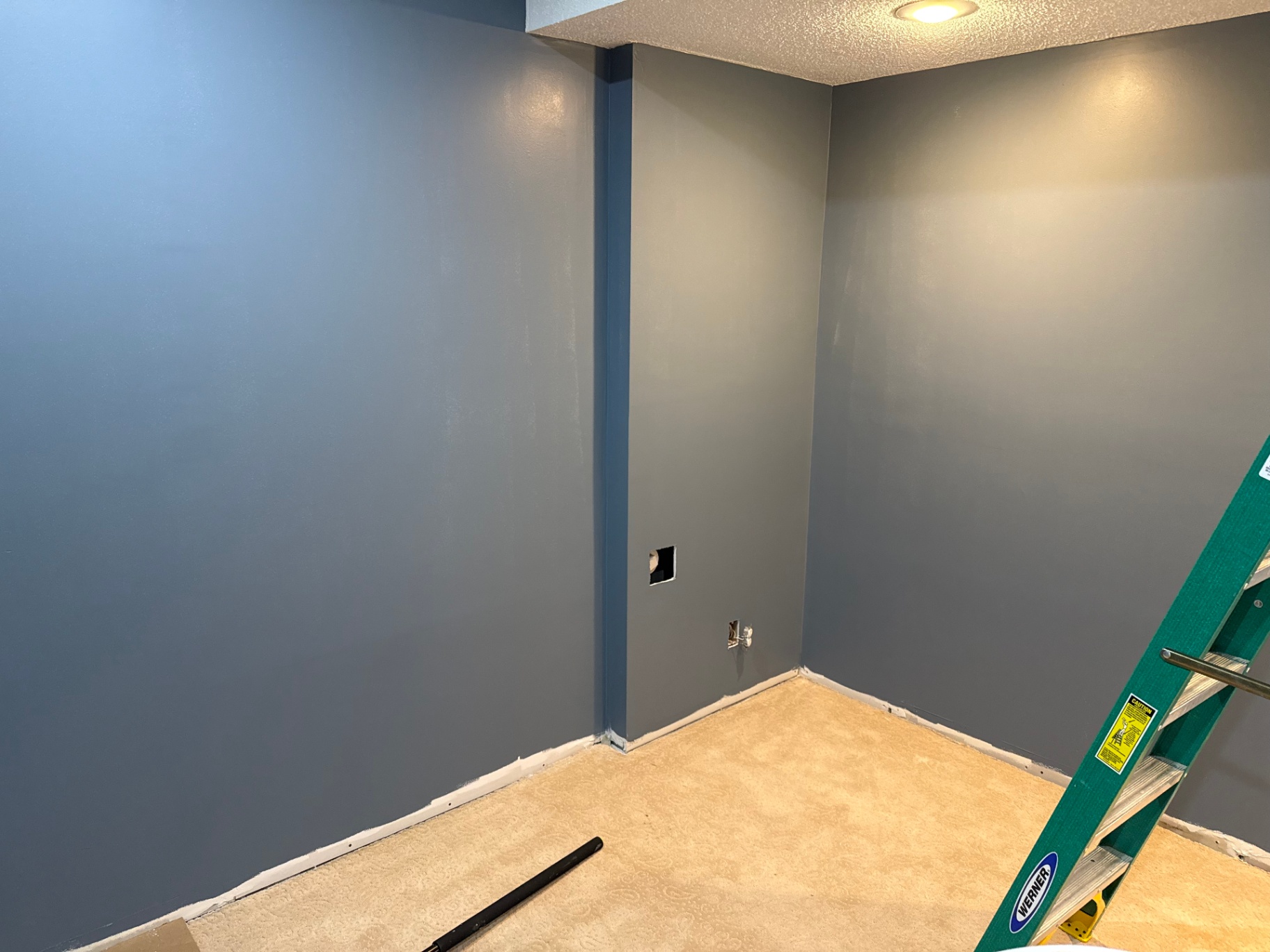 Interior room freshly painted in two shades of blue with crisp white baseboards, textured ceiling, and a work ladder in the corner