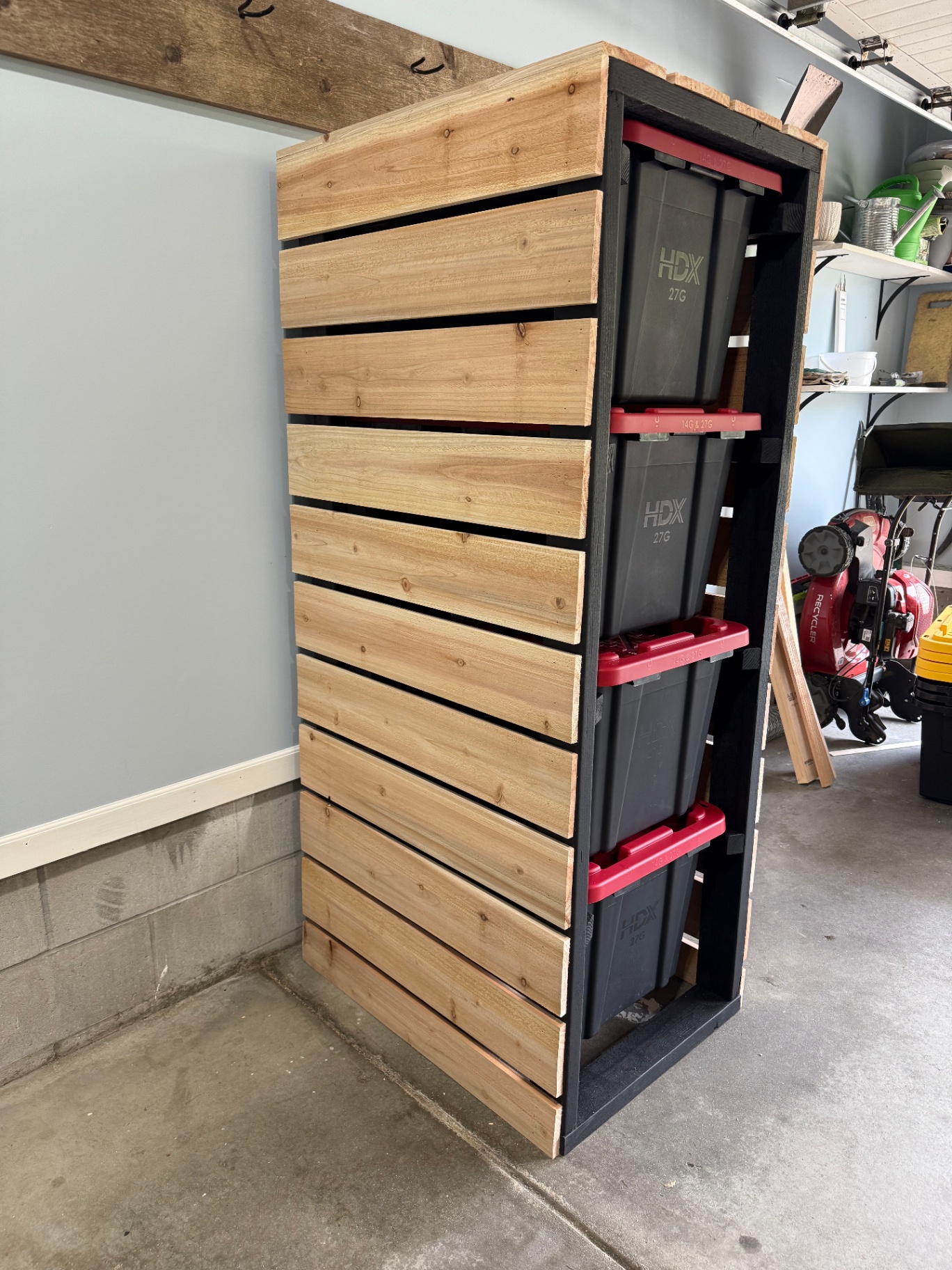 Side view of a custom tote storage rack showing horizontal cedar slat cladding over a black wood frame in a garage