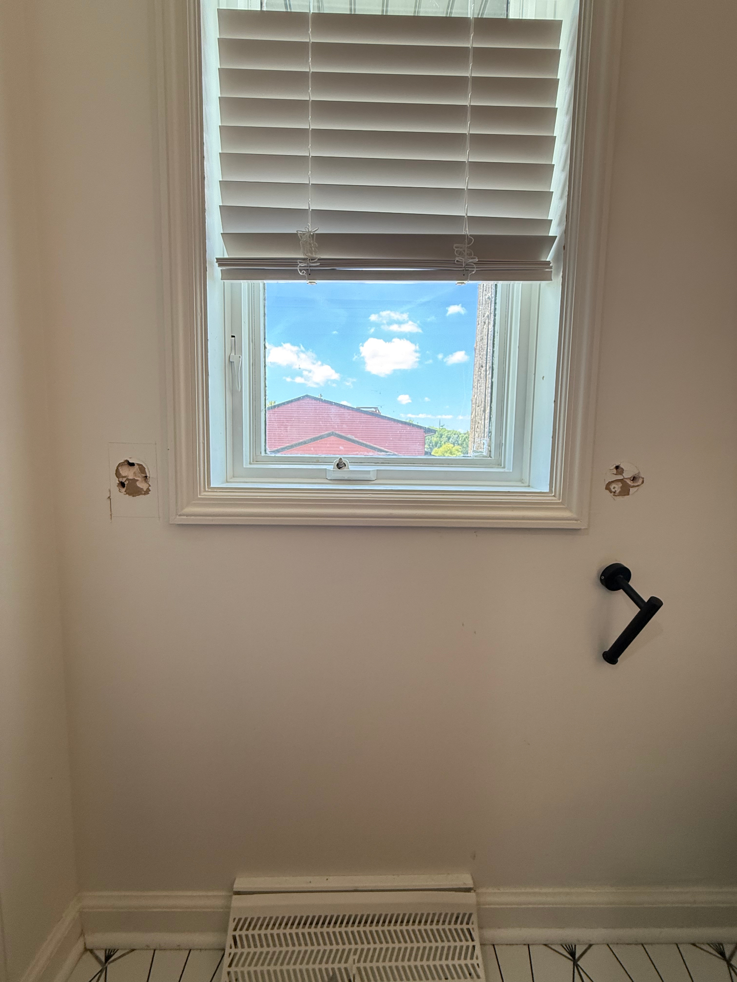 Interior window with white blinds and two small wall openings left behind after old hardware was removed, ready for patching