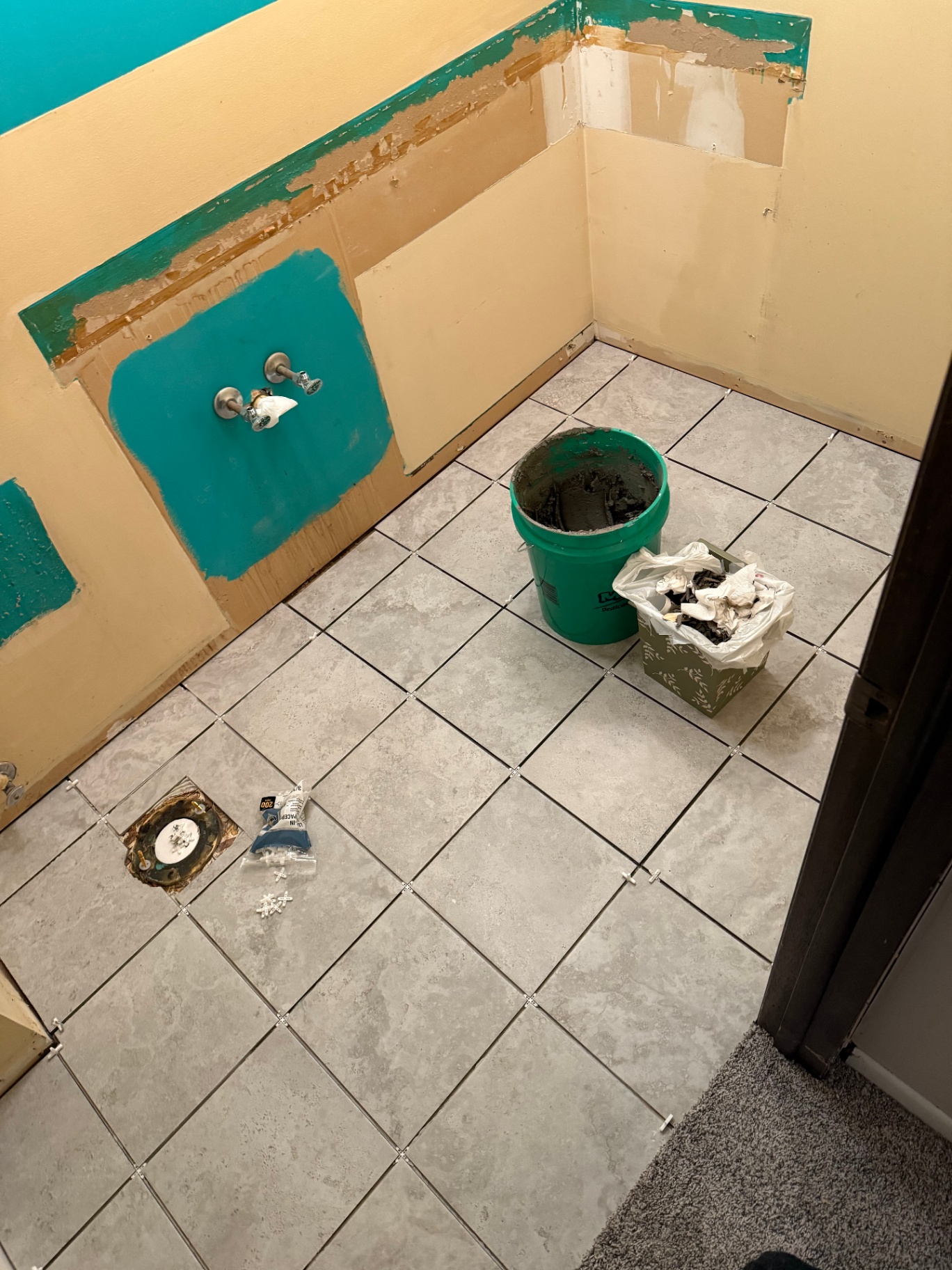Grey stone-look bathroom floor tile freshly set with plastic spacers still in place, next to walls in their original condition