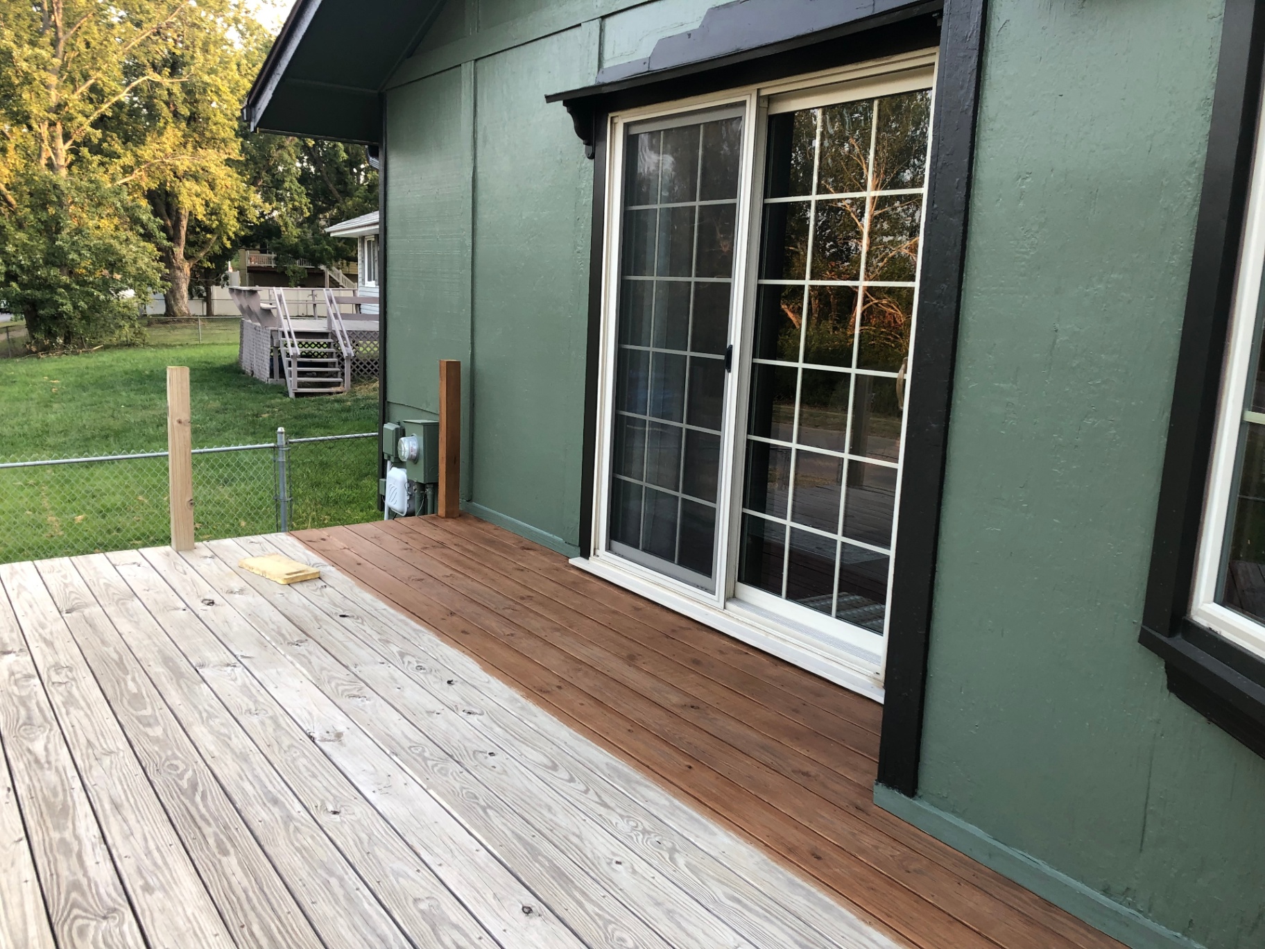 Deck boards mid-restain, with roughly half the boards freshly stained a warm brown and the rest still weathered gray