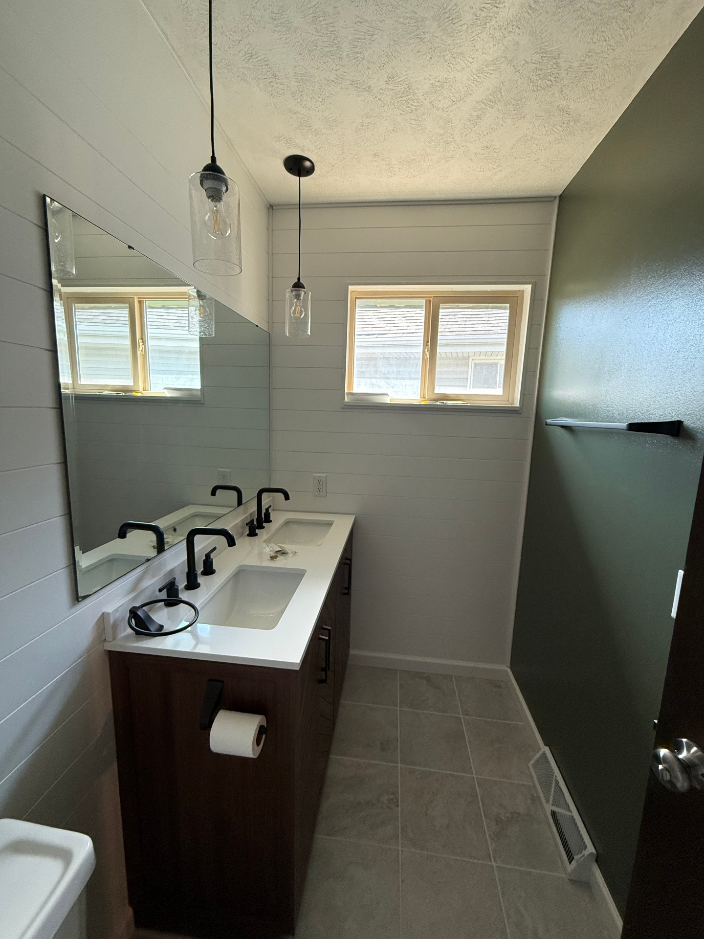 Finished bathroom with a dark wood double vanity, white quartz top, matte black faucets, white shiplap walls, sage green accent wall, tile floor, and glass pendant lights