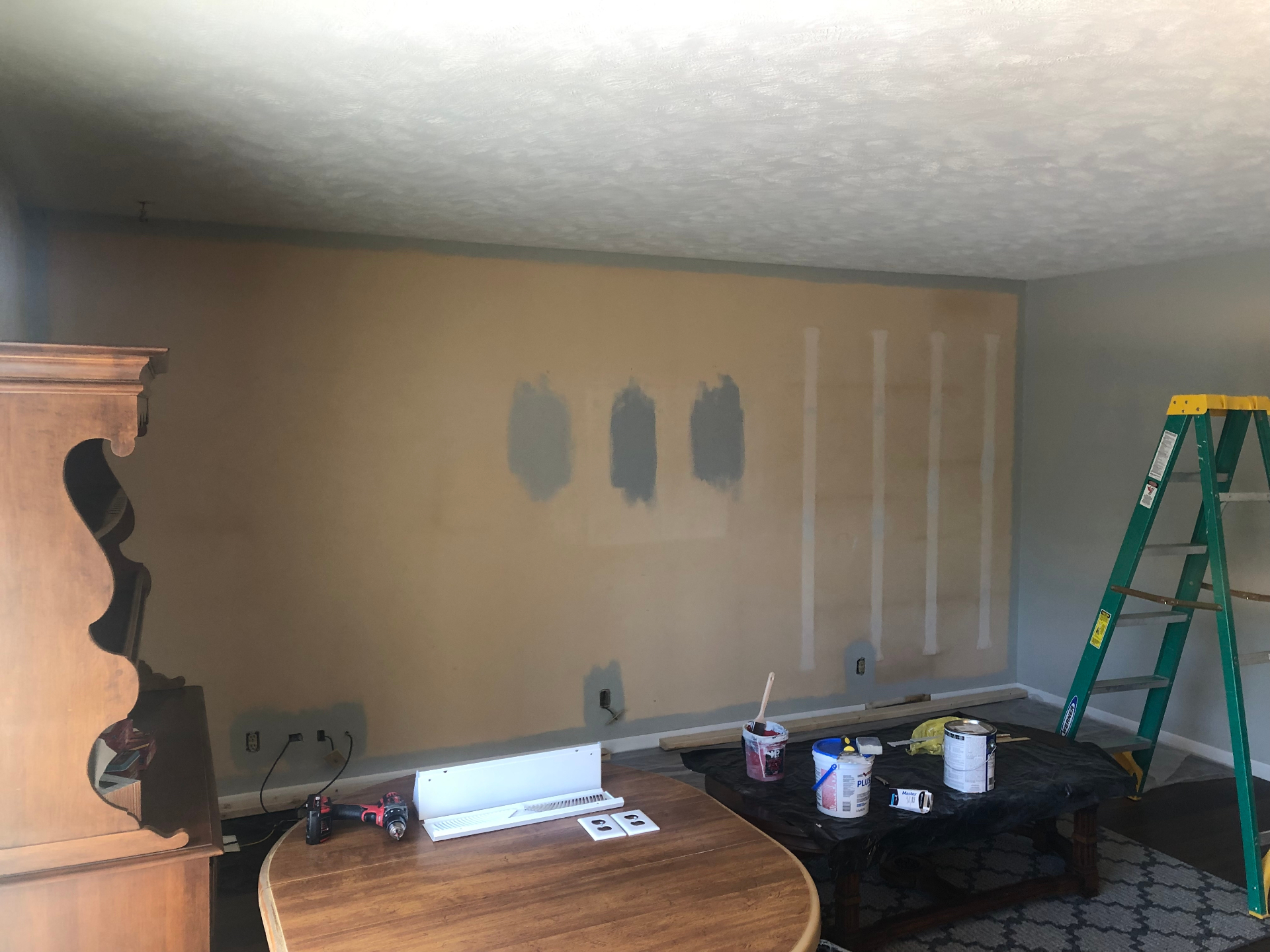 Living room wall during prep with patched areas, paint test swatches, removed trim, and tools staged for the update