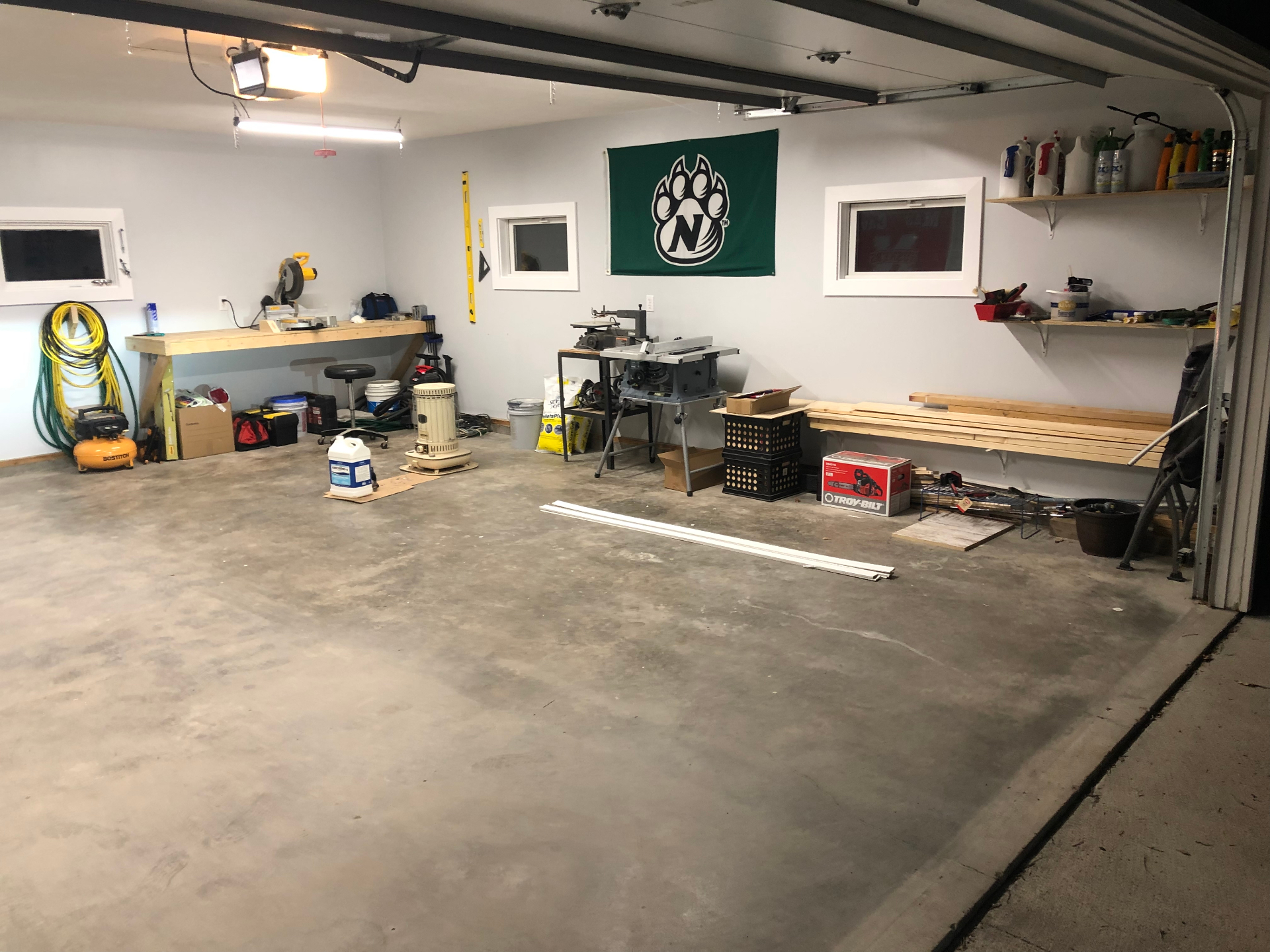 Organized garage workshop with a miter saw station, table saw, wall-mounted shelving, and lumber staged along the wall