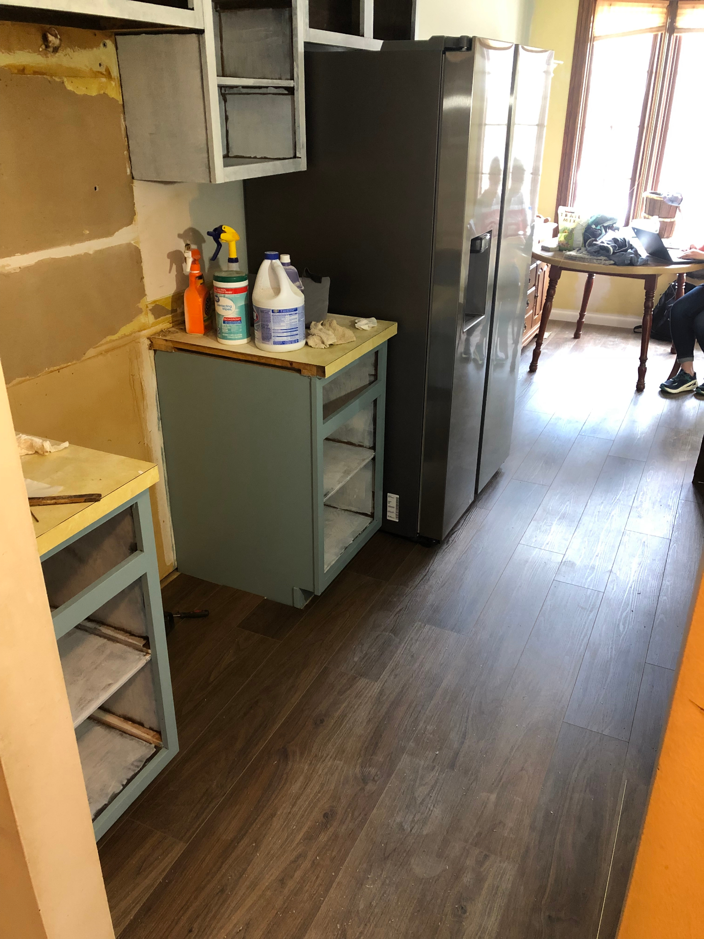 Kitchen during renovation with partially finished cabinet painting, counters in place, and dark wood-look flooring installed