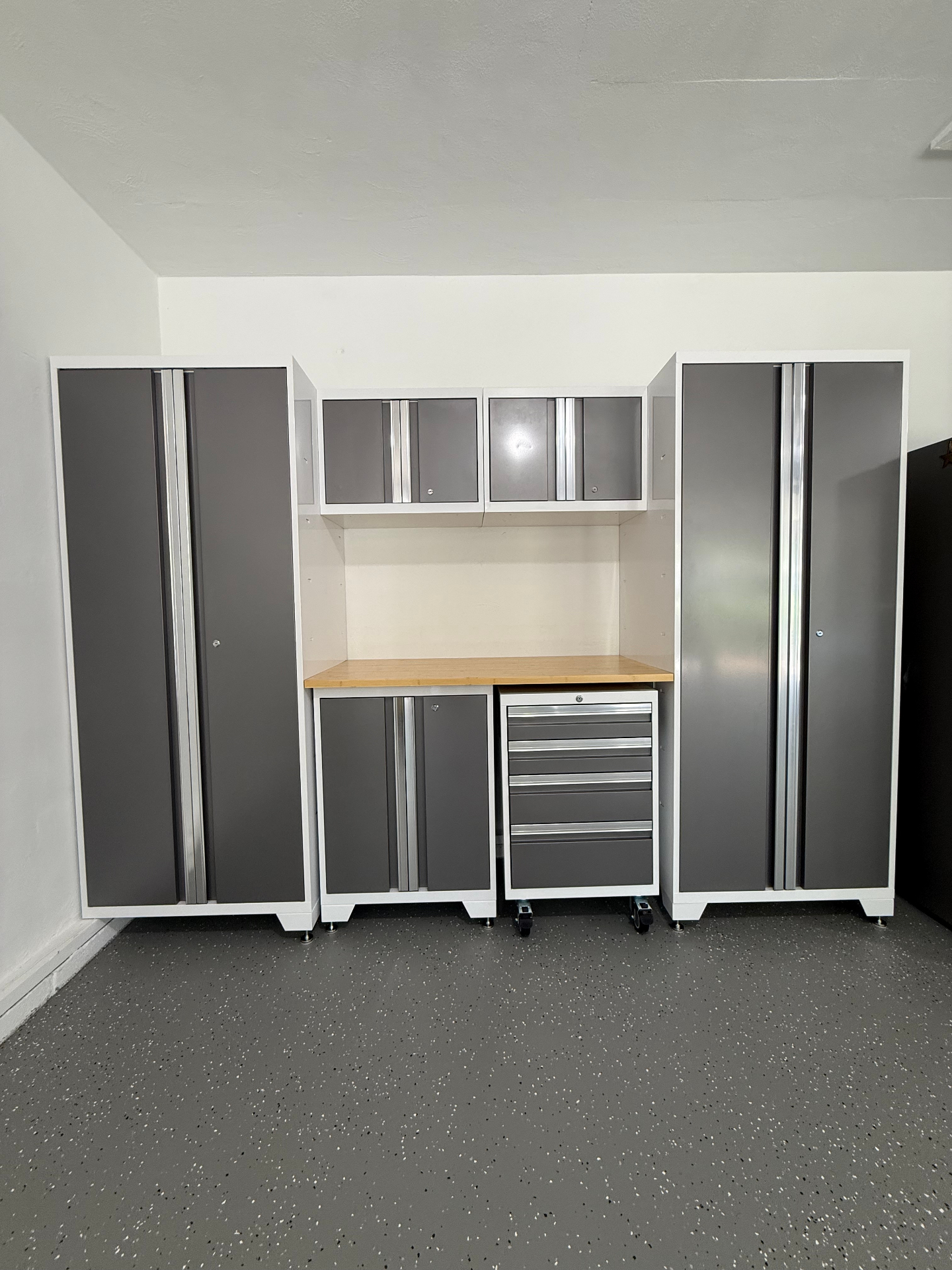 Front view of a fully assembled modular garage cabinet wall with tall lockers, upper cabinets, workbench, and rolling tool chest