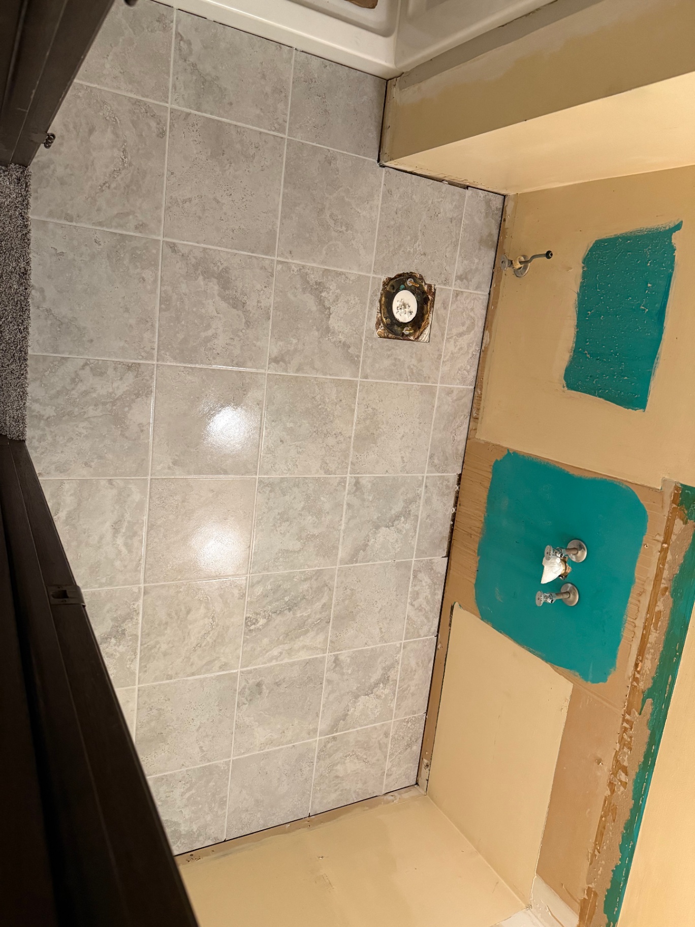 Fresh grey stone-look tile laid on a bathroom wall and floor during installation, next to a wall still in its original condition