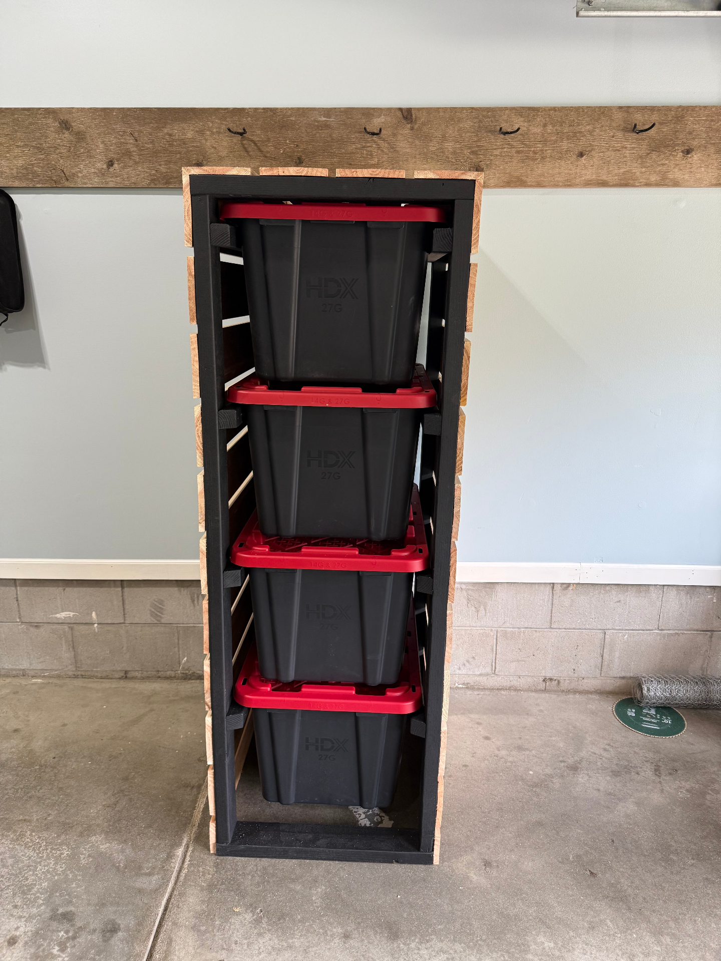 Front view of a custom garage storage rack holding four stacked black totes with red lids inside a black wood frame