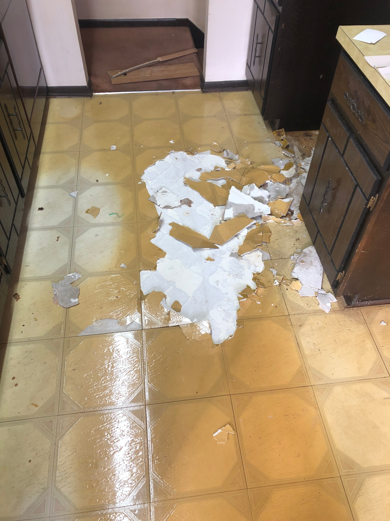 Kitchen floor with damaged yellow sheet flooring being torn out between dark lower cabinets