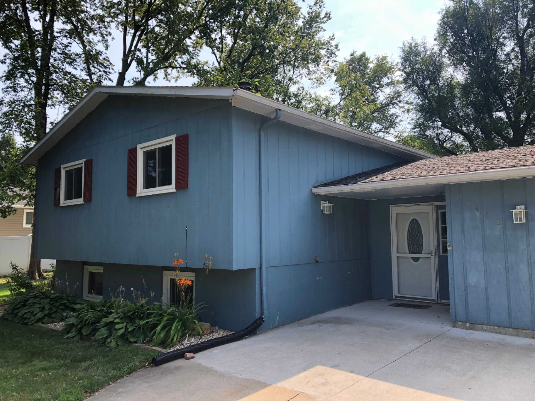 Same split-level home before repainting, with faded medium-blue siding, red shutters, and dated trim
